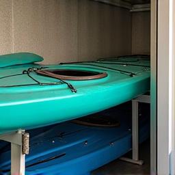 Vandens sporto įranga: baidarės, irklentės, banglentės kabinamos ant sienų sandėlyje.